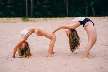 Two flexible sports teenagers girls in swimsuits standing on the beach and male gymnastic bridge...