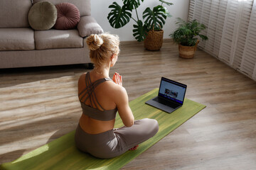 Sporty adult woman teaching yoga in an online class. Fit middle aged yogini live streaming hatha...
