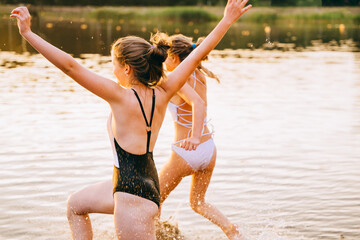Happy teens run from the shore into the water. Summer children's vacation on shore of a lake or...