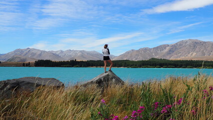 Lake Tekapo. Tekapo, New Zealand.

Young lady standing on a rock admiring the beautiful view of Lake Tekapo and surrounding mountain ranges.
