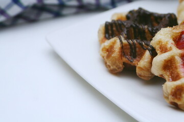 Waffles topped with chocolate and strawberries served in a white plate.