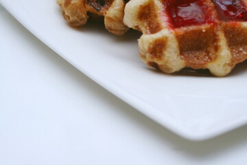 Waffles topped with chocolate and strawberries served in a white plate.