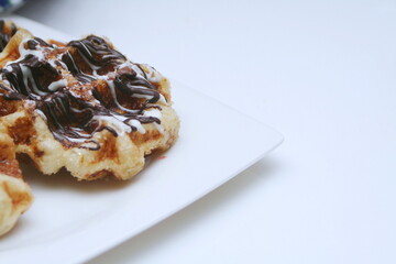 Waffles topped with chocolate and strawberries served in a white plate.