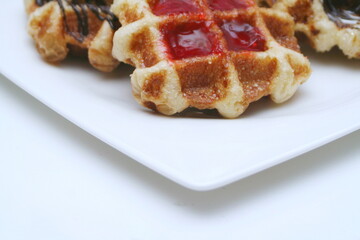 Waffles topped with chocolate and strawberries served in a white plate.