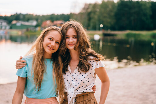 Vacation, relax, active lifestyle concept. Two teenager girls friends having fun, laughing, hugging standing at nature by the lake.