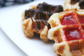 Waffles topped with chocolate and strawberries served in a white plate.