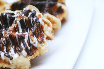 Waffles topped with chocolate and strawberries served in a white plate.