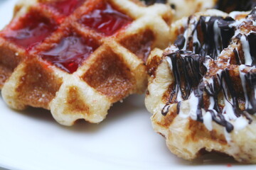 Waffles topped with chocolate and strawberries served in a white plate.
