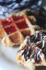 Waffles topped with chocolate and strawberries served in a white plate.