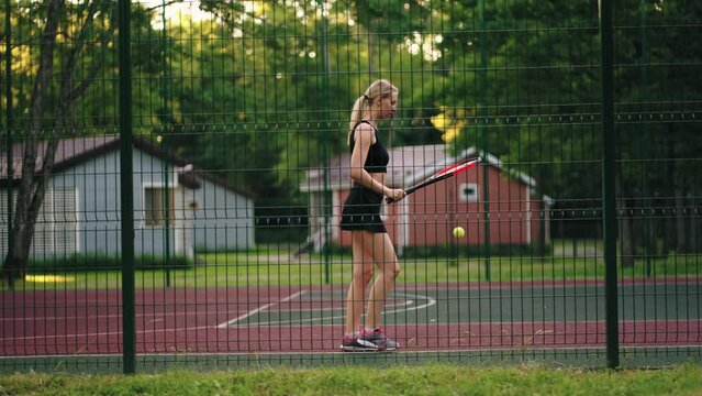 young sportswoman is training on tennis court, bouncing ball by racket, athletic blonde lady