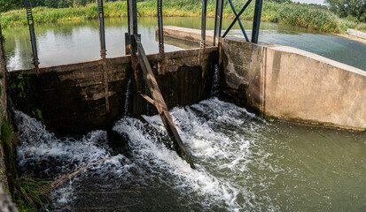Śluza znajdująca się na małej rzeczce w obszarze wiejskim w otoczeniu zarośli w porze letniej
