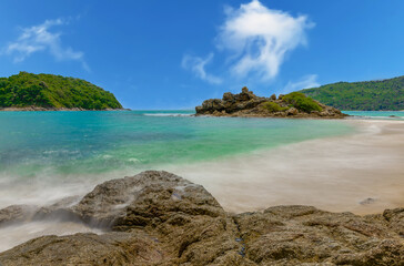 Fototapeta premium Long exposure of waves crashing on the rocks with beautiful island and mountains in Background. photographed in Naiharn Nai Harn Beach Phuket Thailand