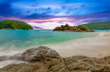 Long exposure of waves crashing on the rocks with beautiful island and mountains in Background. photographed in Naiharn Nai Harn Beach Phuket Thailand