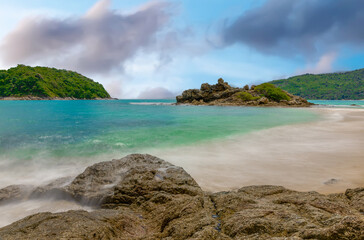 Fototapeta premium Long exposure of waves crashing on the rocks with beautiful island and mountains in Background. photographed in Naiharn Nai Harn Beach Phuket Thailand