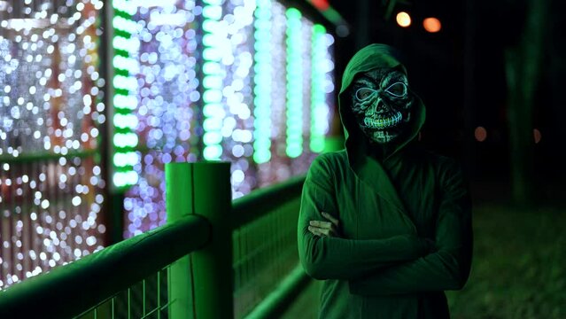 A woman with a death mask with neon glow dancing in an amusement park at night. Theme of costumes and reincarnations for Halloween