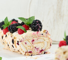Baked meringue roll with cream and fresh fruits on a white wooden board, delicious dessert