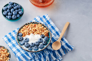 Breakfast with granola, blueberry, yogurt and honey. Bowl with granola and berries on blue napkin. Delicious and healthy breakfast concept. Top view. Copy space
