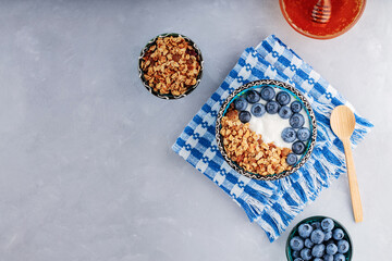 Breakfast with granola, blueberry, yogurt and honey. Bowl with granola and berries on blue napkin. Delicious and healthy breakfast concept. Top view. Copy space