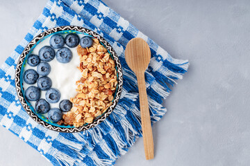 Breakfast with granola, blueberry, yogurt and honey. Bowl with granola and berries on blue napkin. Delicious and healthy breakfast concept. Top view. Copy space