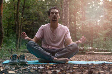 Young handsome man doing yoga in lotus position in the wood. Training and sport on nature concept