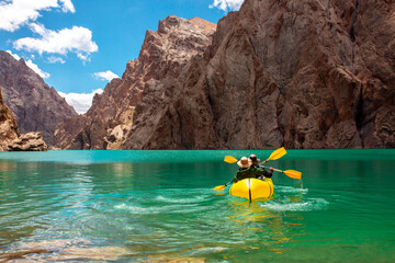 Kayaking on a mountain lake. Two men are sailing on a yellow canoe along the lake along the rocks. The theme of water sports and summer holidays.
