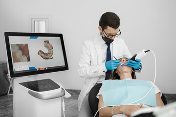 Male orthodontist scaning patient with dental intraoral scanner and controls process on screen.
