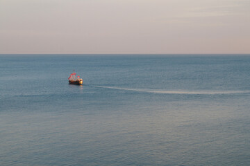 A small ship is moving on the surface of a calm sea towards the horizon.