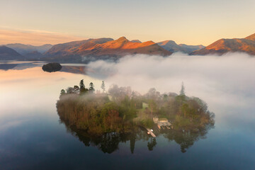 Aerial drone photograph of Derwent Island with Lake District mountains in background at dawn. Calm and misty landscapes. Derwentwater, Cumbria, UK. - 524676617