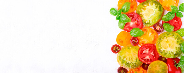 Web banner with slices of assorted tomatoes of different colors and sizes and basil leaves on white table. Food background. Mockup with copy space