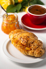 Croissant with orange jam on a white plate