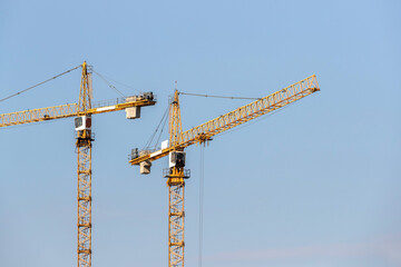 Two yellow construction tower cranes against the blue sky