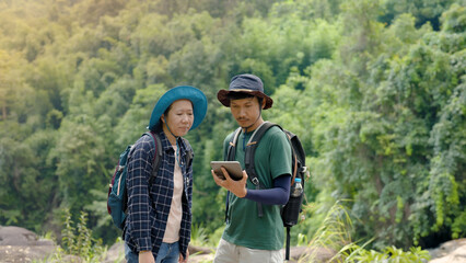 Two Asian lovers,walk and stand on a large rock,And the two of them looked at the direction of their walk and used both hands to point to the path, and looked for the path, eagerly.