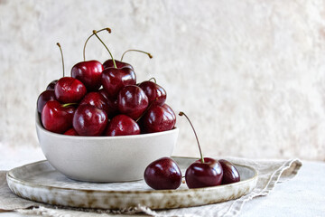 Fresh cherries in a ceramic plate stand on a linen napkin. Red cherry berries on a light background. Selective focus. The concept of healthy eating.