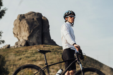 Portrait of Professional Equipped Cyclist on Trail with Giant Stone on the Background, Adult Man...