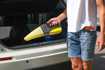 man holding a handy vacuum cleaner on the background of the car