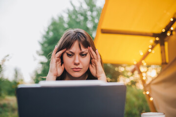 Tired Woman freelancer  using a laptop on a cozy glamping tent in a sunny day. Luxury camping tent for outdoor summer holiday and vacation. Lifestyle concept