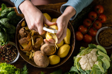 A woman is peeling potatoes. Various fresh vegetables lie on the table. Cooking vegetarian food.