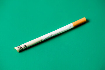 Smoking and money. Rolled up dollar bill in a cigarette. Green background. The high cost of smoking cigarettes concept.