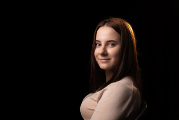 Fototapeta premium Portrait of a young woman on a dark background. The girl in the brown sweater. Friendly face looking at the camera. Place for text.