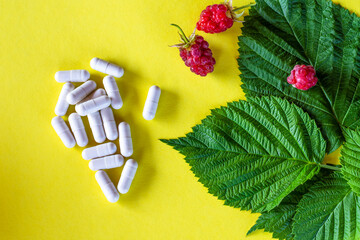 Pills (drugs), raspberry leaves and berries on a yellow background. The concept of treatment of seasonal diseases. Traditional and folk medicine