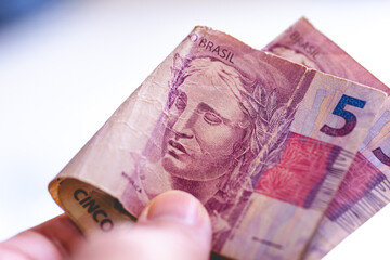 Um homem segurando na mão notas do Real Brasileiro - BRL no valor de 5 reais. Conceitos de...