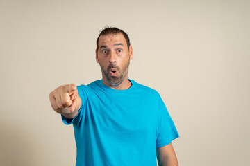 Bearded latin man in blue t-shirt pointing his finger at you camera gesture isolated on beige wall...