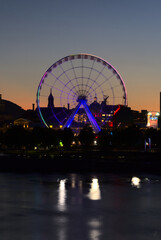 Long exposure of Montreal Grand Ferris Wheel in Old Port with motion blurat twilight blue hour. Reflections of sun rays on Saint Laurent river with a background of cloudy blue sky