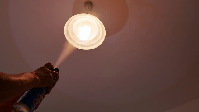 hand using mosquito insecticide spray to kill flies and mosquitoes. clearly visible backlight spray with droplets.