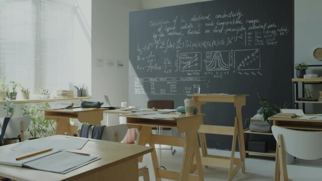 Zoom In Shot Of College Classroom With Desks And Chalkboard With Math Formulas On It, No People There