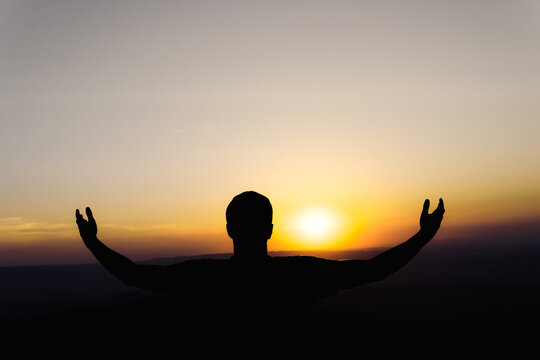 Sunset with a silhouette of a young man in an attitude of gratitude to the sun