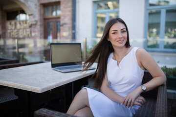 Portrait of a young happy woman in a cafe sitting at a laptop. Talk on mobile phone