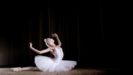 in rays of spotlight, on the stage of the old theater hall. Young ballerina in suit of white swan...