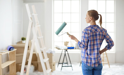 Beautiful young woman doing wall painting, standing near ladder