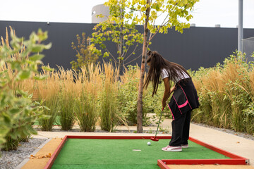 Cute little girl playing mini golf in a park. - obrazy, fototapety, plakaty
